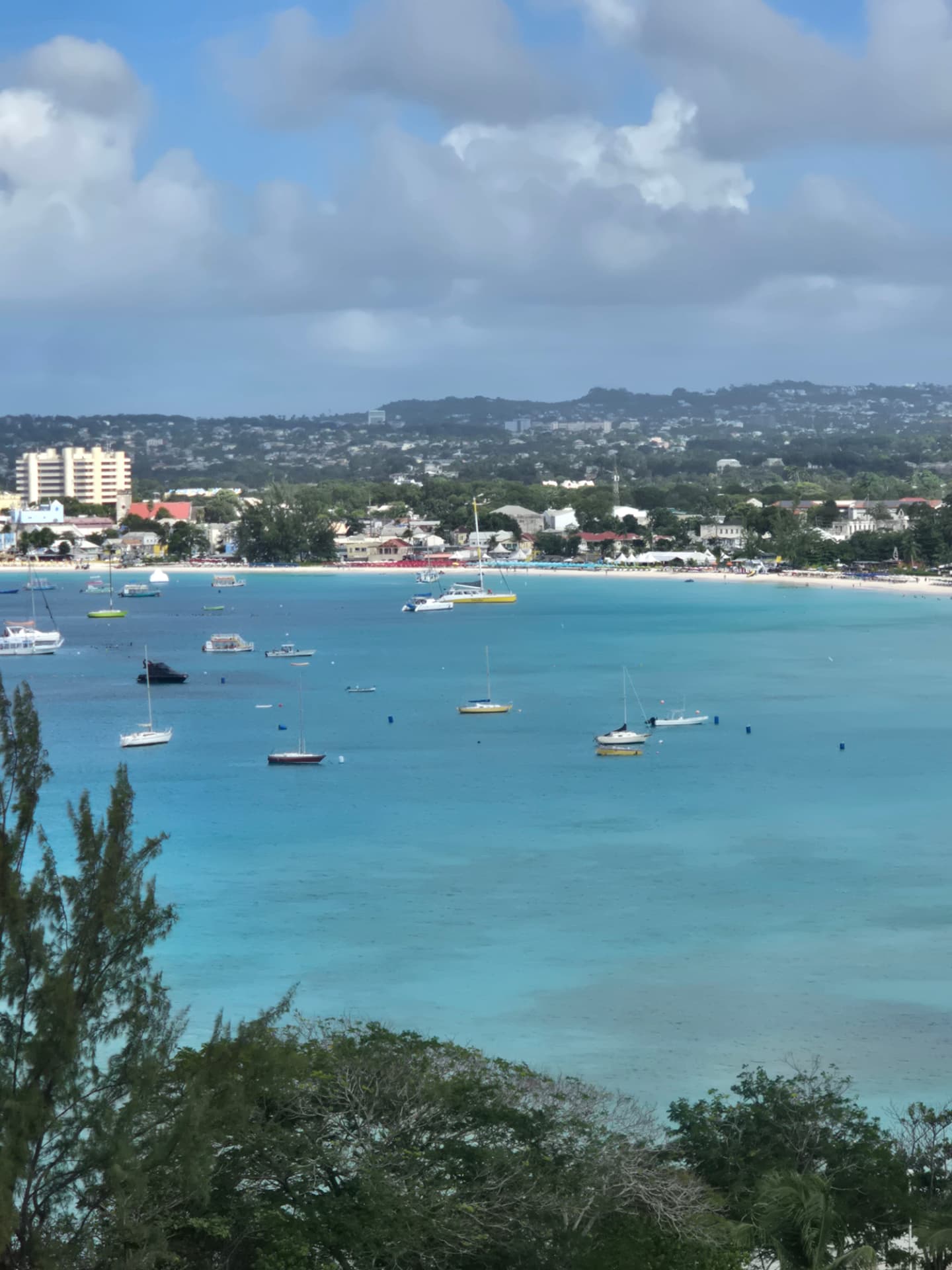 Turquoise Carlisle Bay in Barbados seen from a hill, sailboats at anchor off a long white beach and town.