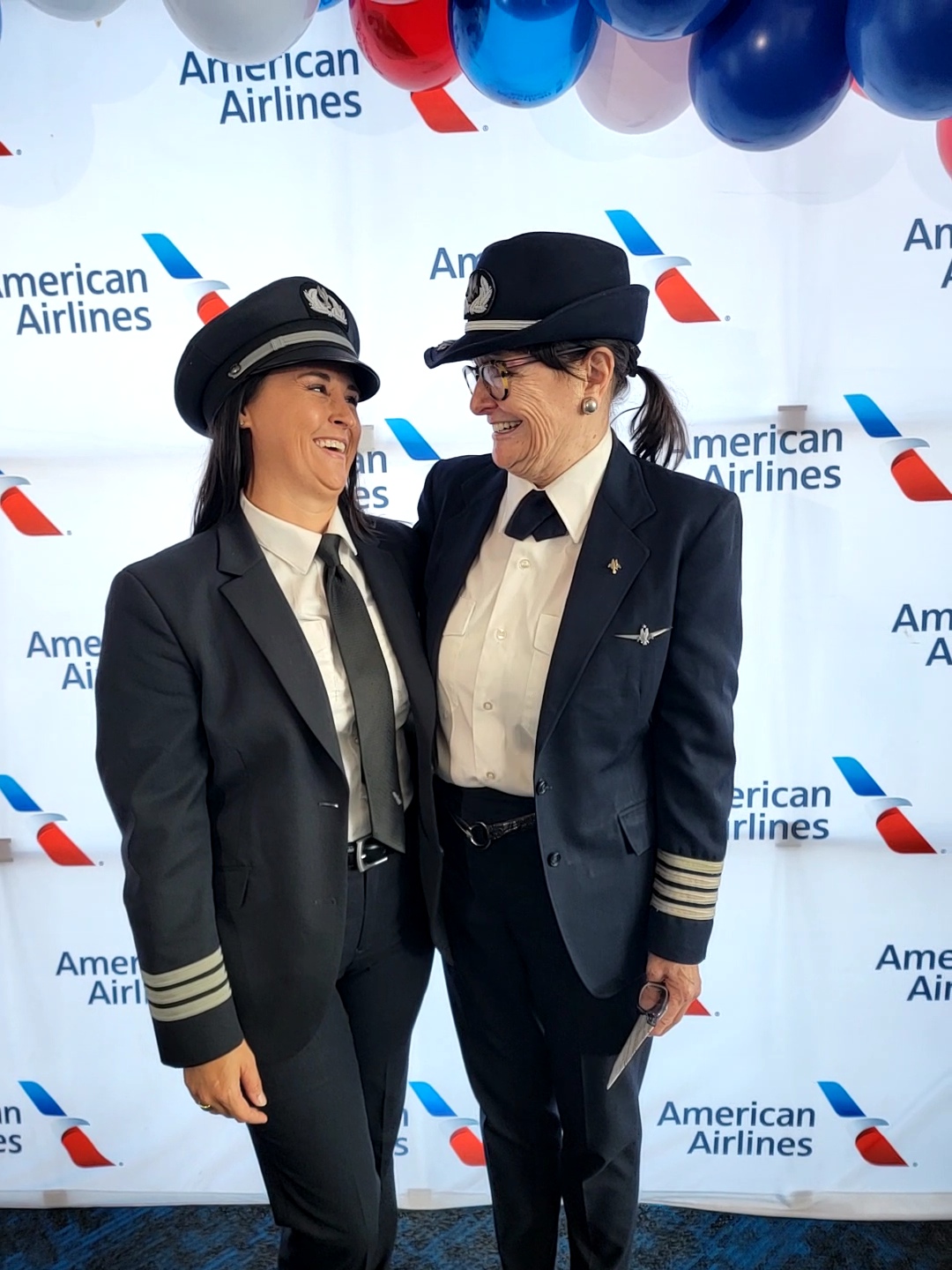 Nikki and Bonnie Tiburzi in American Airlines captain uniforms, laughing together.