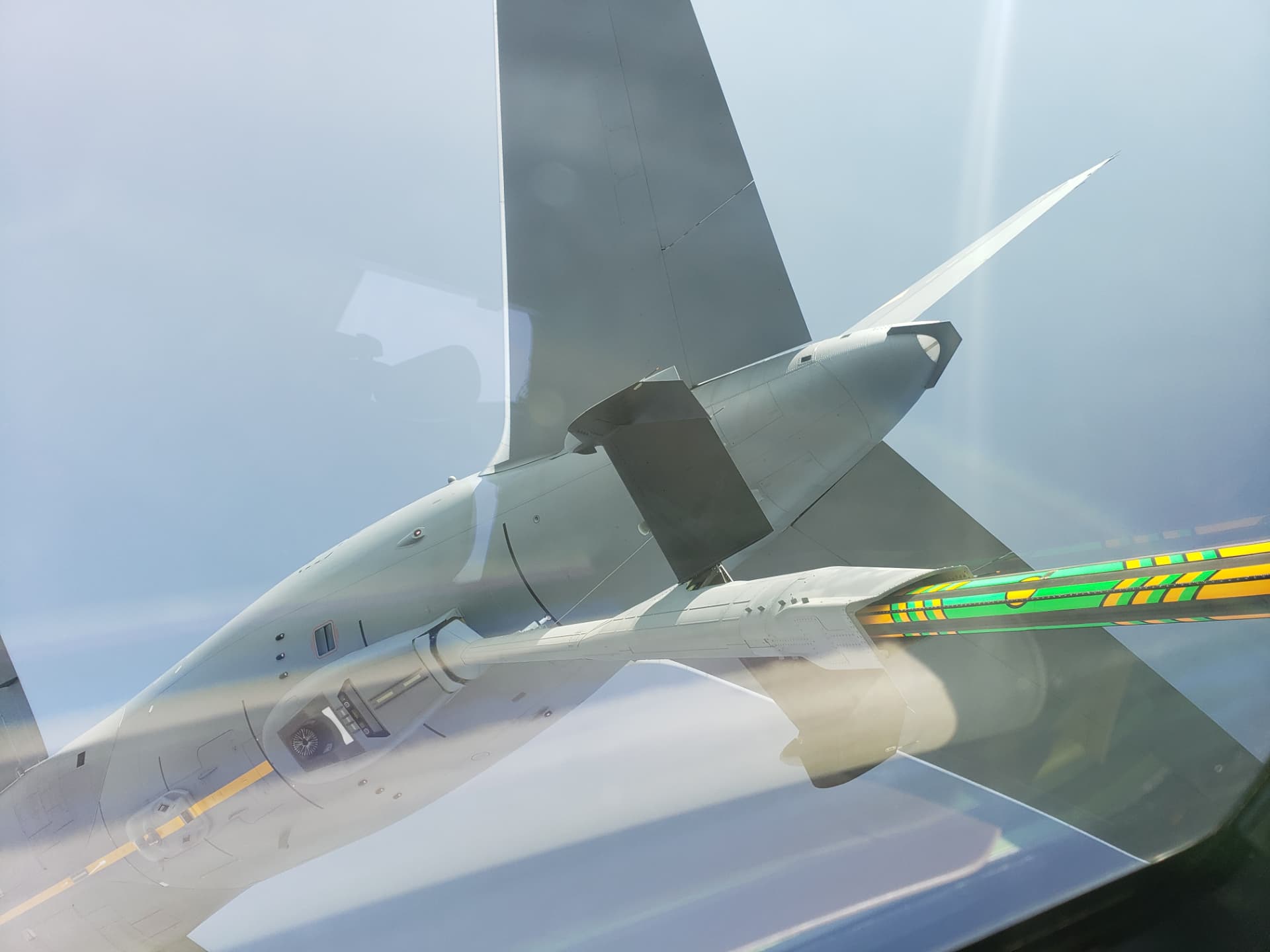 The striped refueling boom and tanker tail seen through the receiver's windscreen.