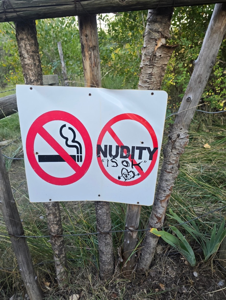 A hand-painted sign on a wooden fence: no smoking, and nudity crossed out as okay.