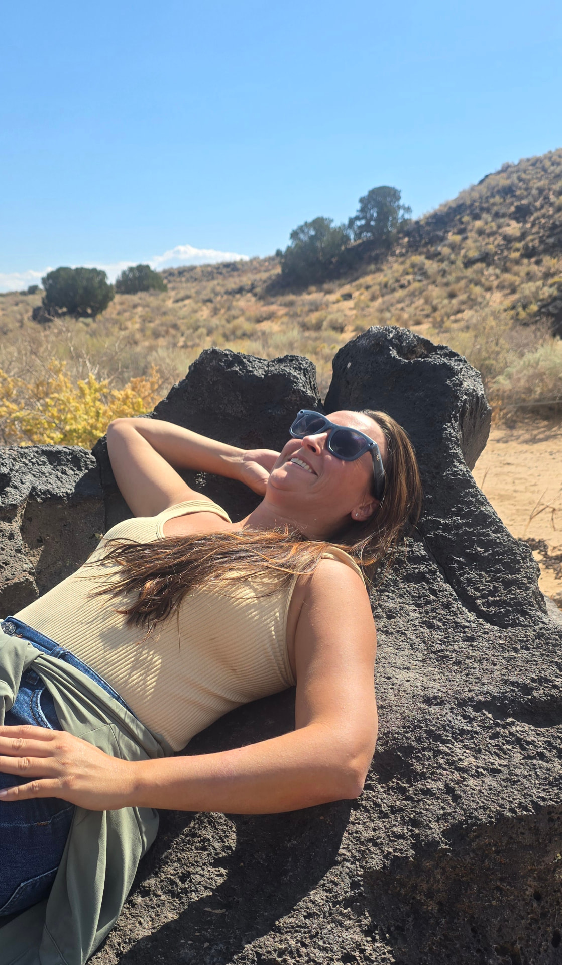 Nikki Bodie laughing while reclining on black lava rock in the high desert under a clear blue sky.